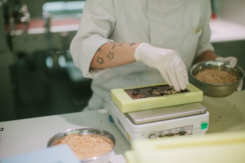 Close-up of a chocolatier adding toppings to a chocolate bar in a confectionery kitchen.